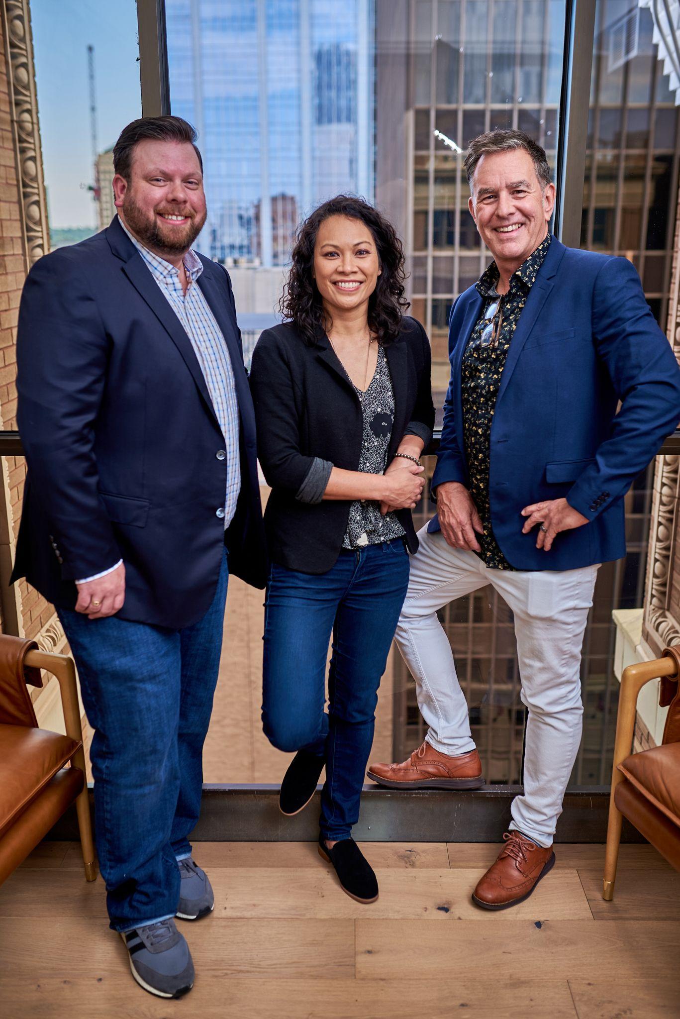 Three colleagues standing by a window with a city view behind them — Team photography, Austin Three colleagues standing by a window with a city view behind them
