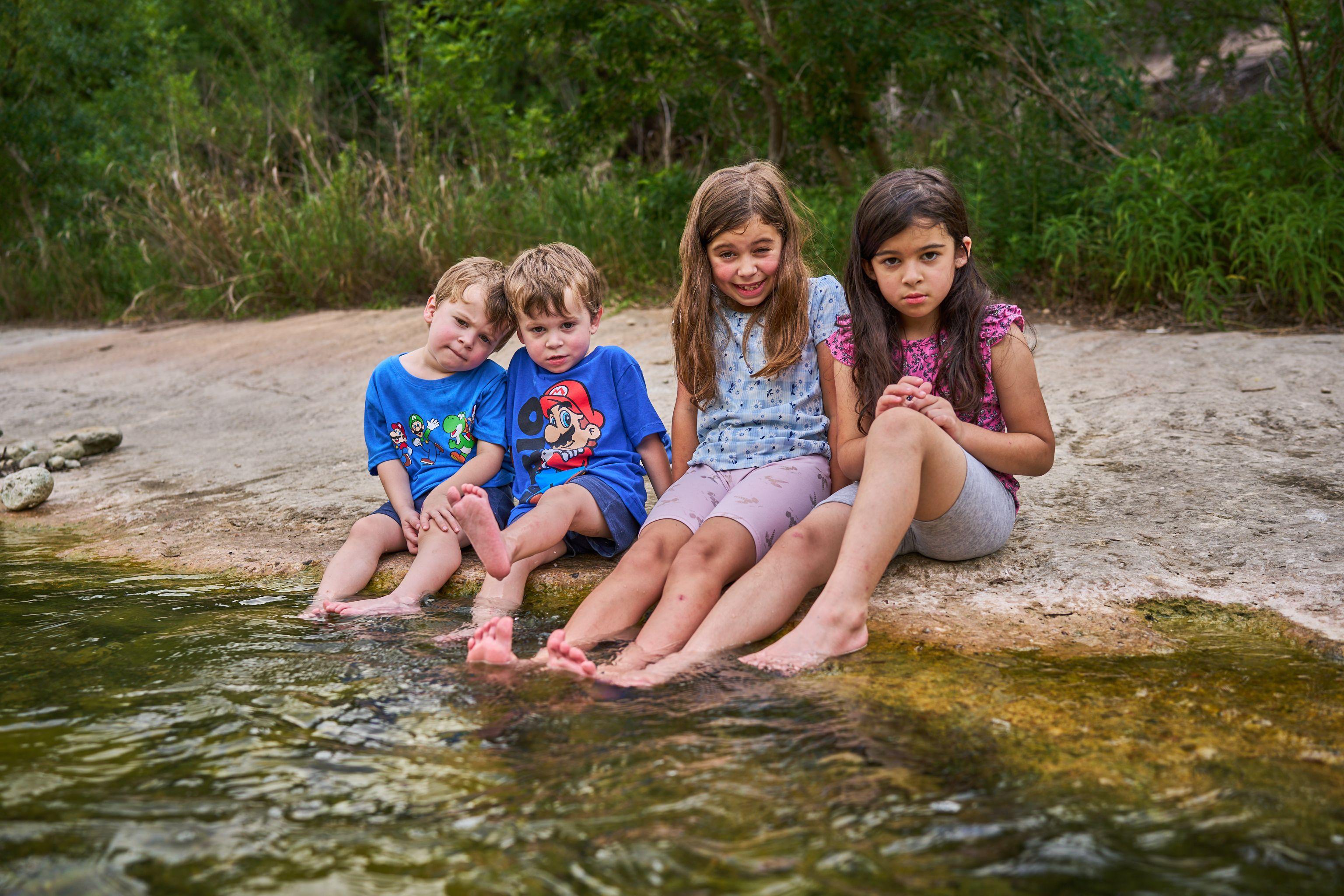 Four children sitting on a rock ledge with their feet in the creek — Bull Creek District Park photography, Austin Four children sitting on a rock ledge with their feet in the creek.