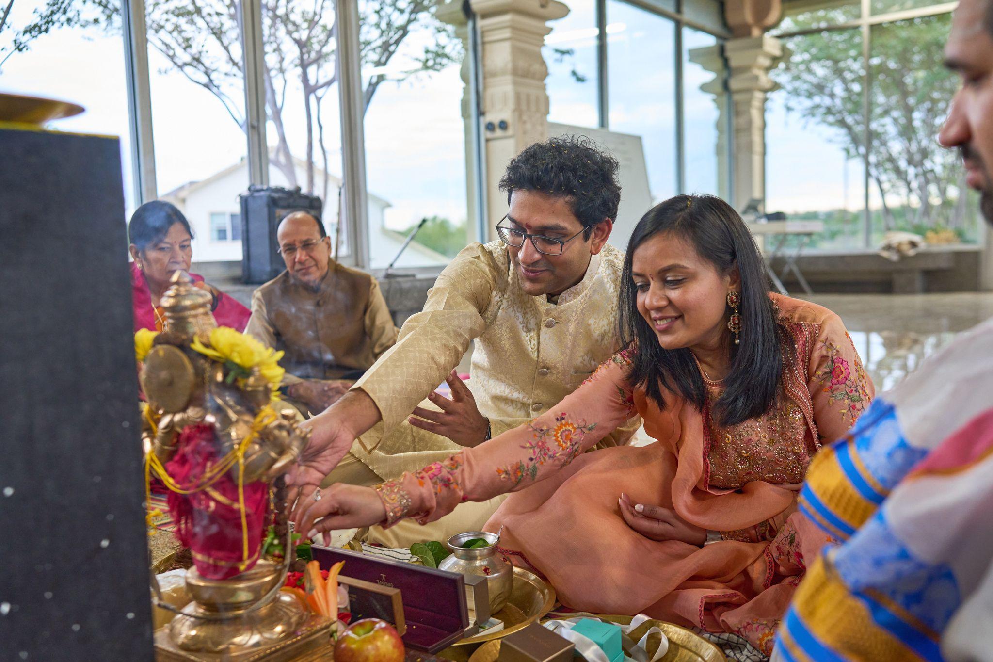 Couple performing a puja together at a low decorated table, marigolds and brass vessels — Religious Ceremonies photography, Austin A couple performing a puja together at a low decorated table, marigolds and brass vessels in front of them.
