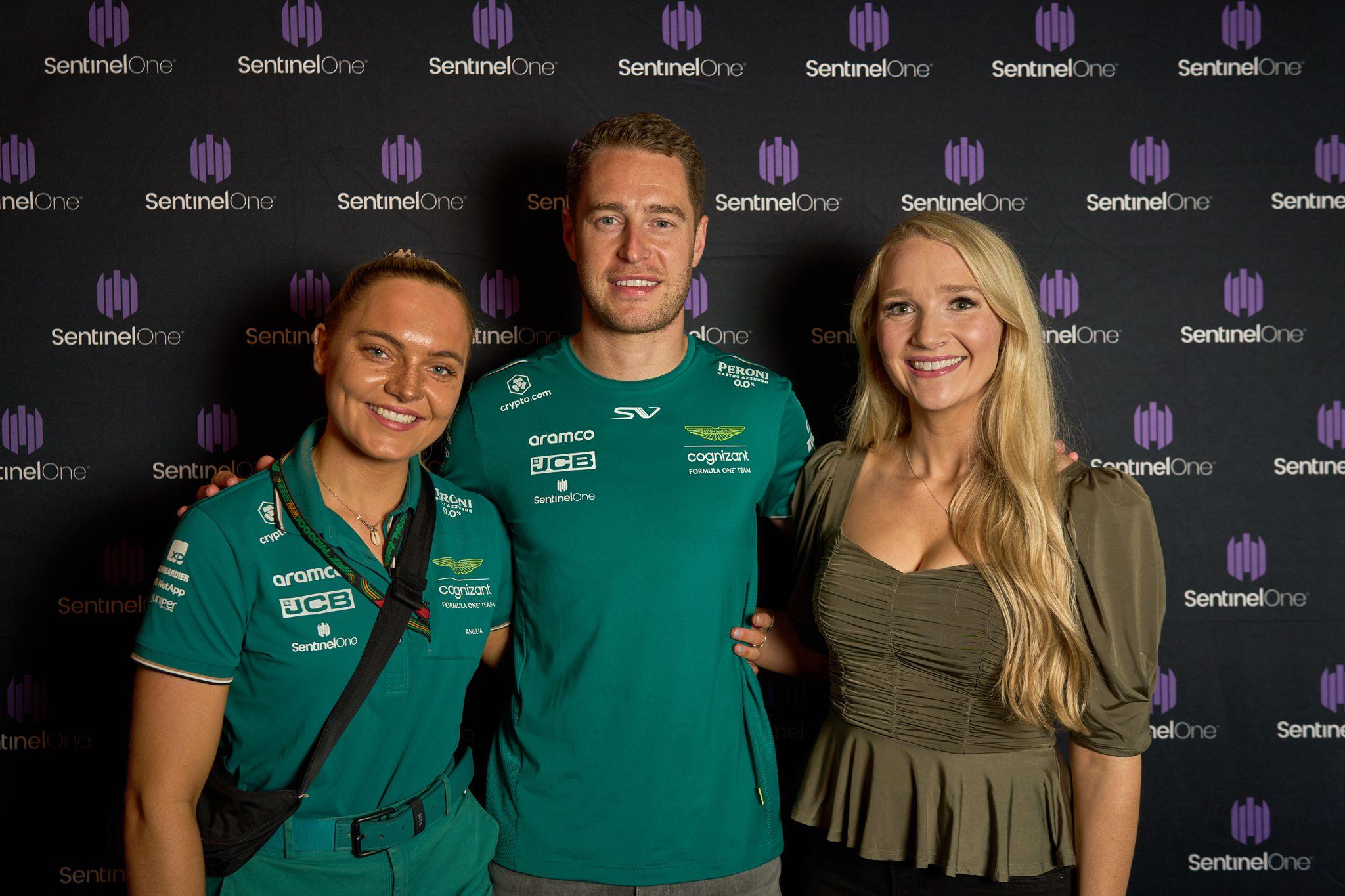 Two brand hosts flanking an Aston Martin Formula 1 driver for a portrait — Brand Collaborations photography, Austin Two brand hosts flanking an Aston Martin Formula 1 driver for a portrait on the SentinelOne sponsor wall.