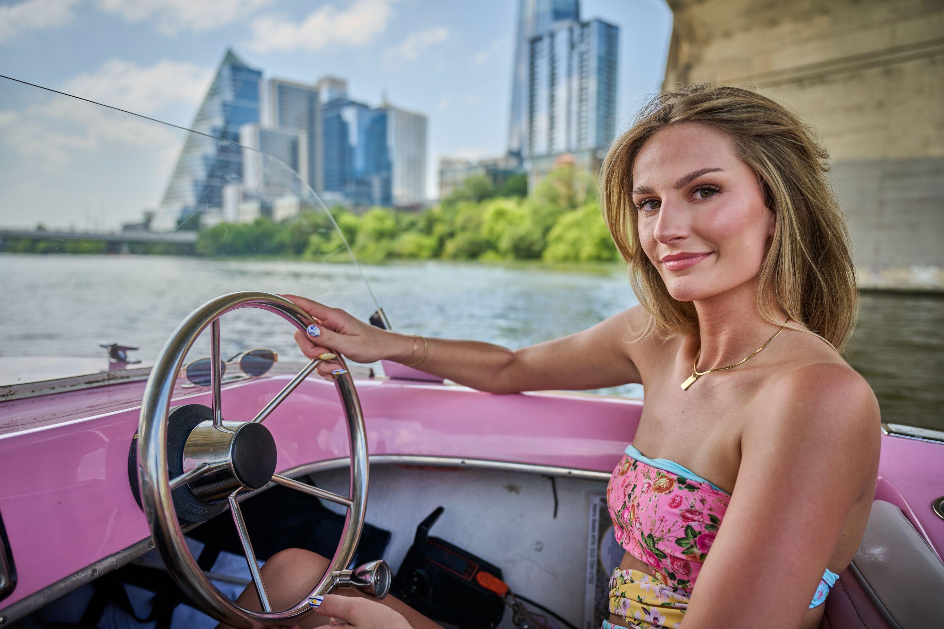 Woman at the wheel of a pink vintage boat on the water — Bachelor & Bachelorette photography, Austin A woman at the wheel of a pink vintage boat on the water.