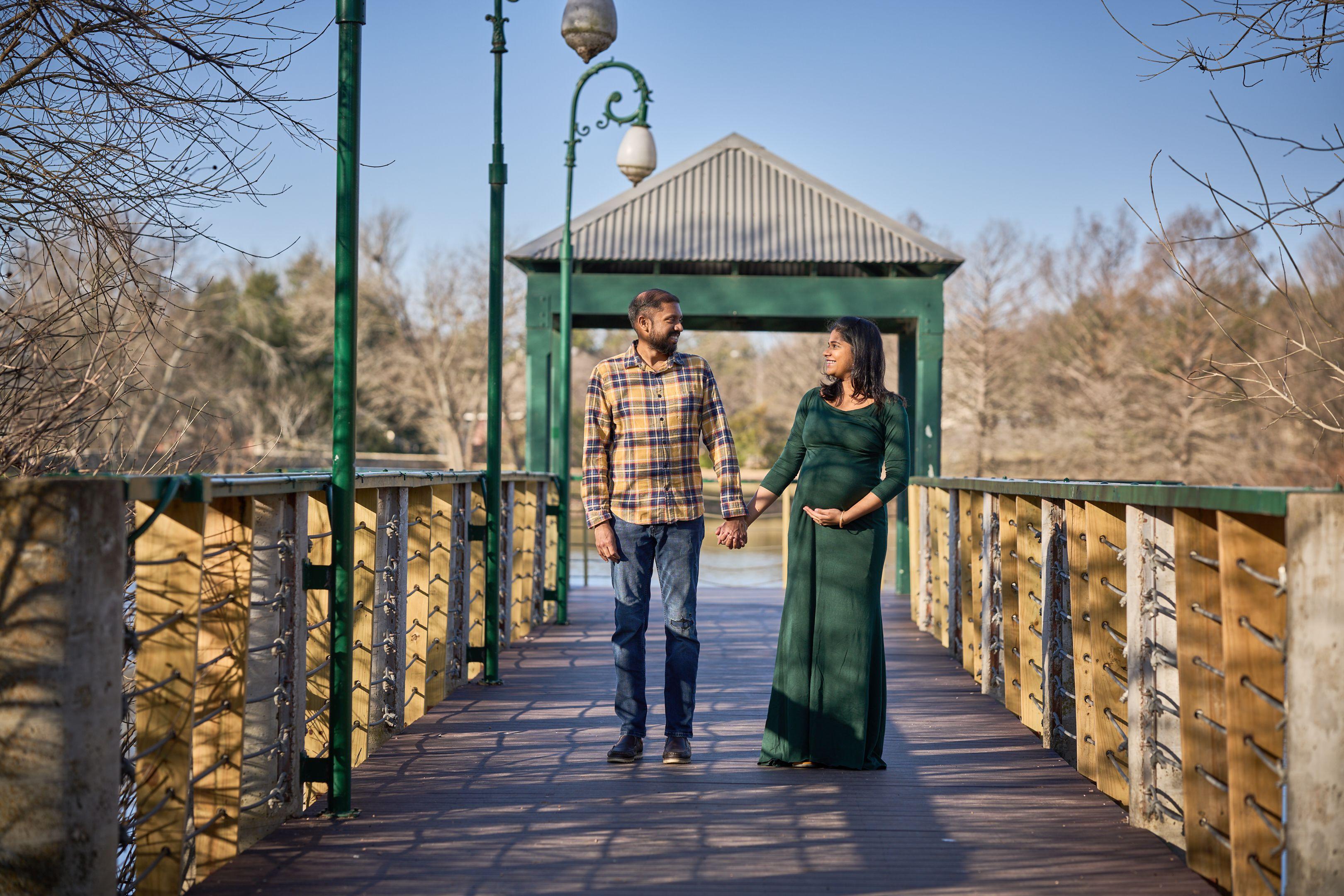 Expectant couple holding hands on the boardwalk that runs out to the Mills Pond pavilion — Mills Pond photography, Austin An expectant couple holding hands on the boardwalk that runs out to the Mills Pond pavilion