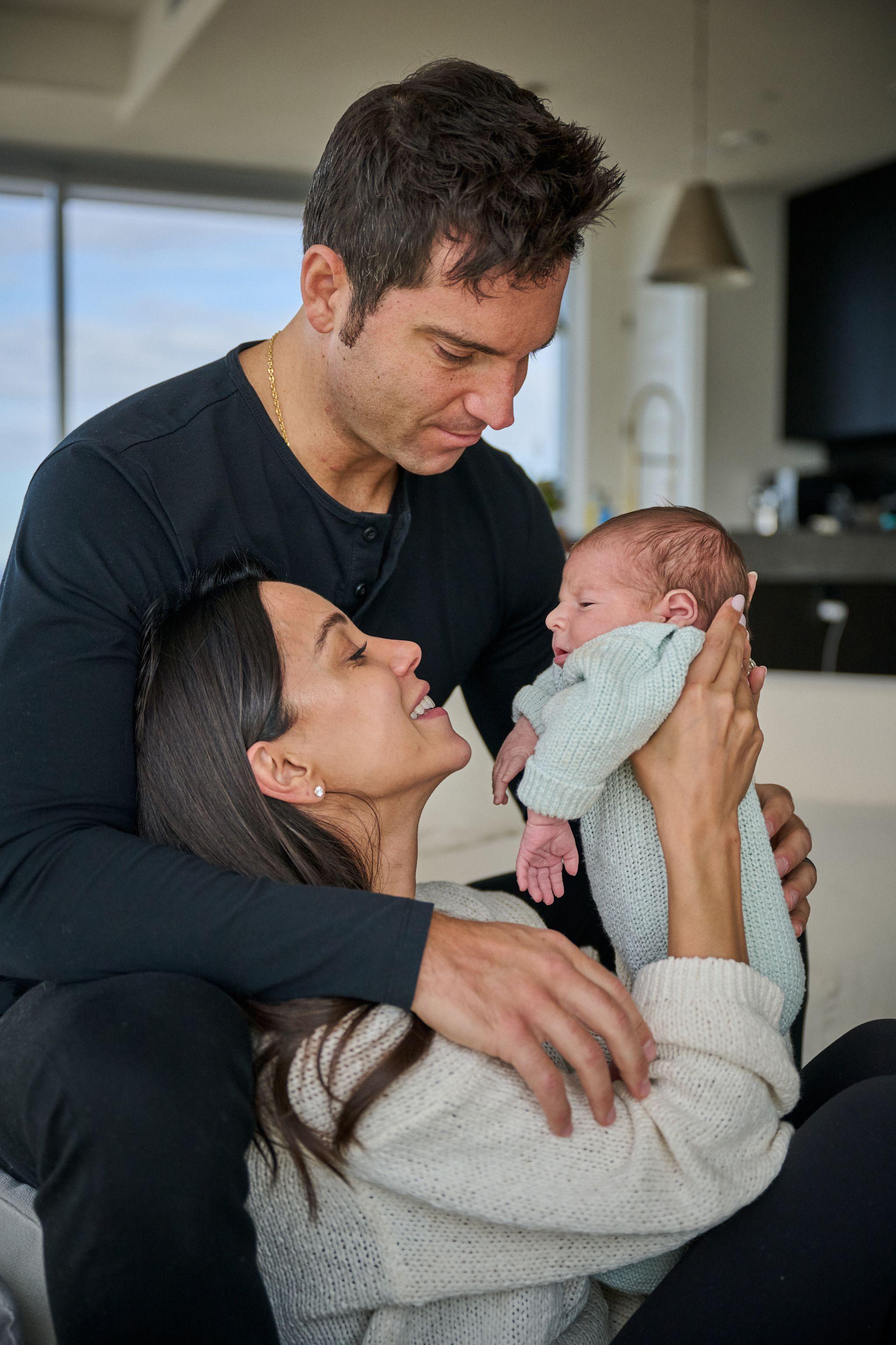 Mother lying back in her partner's arms holding their newborn, both looking down at the baby — Newborn photography, Austin A mother lying back in her partner's arms holding their newborn, both looking down at the baby.