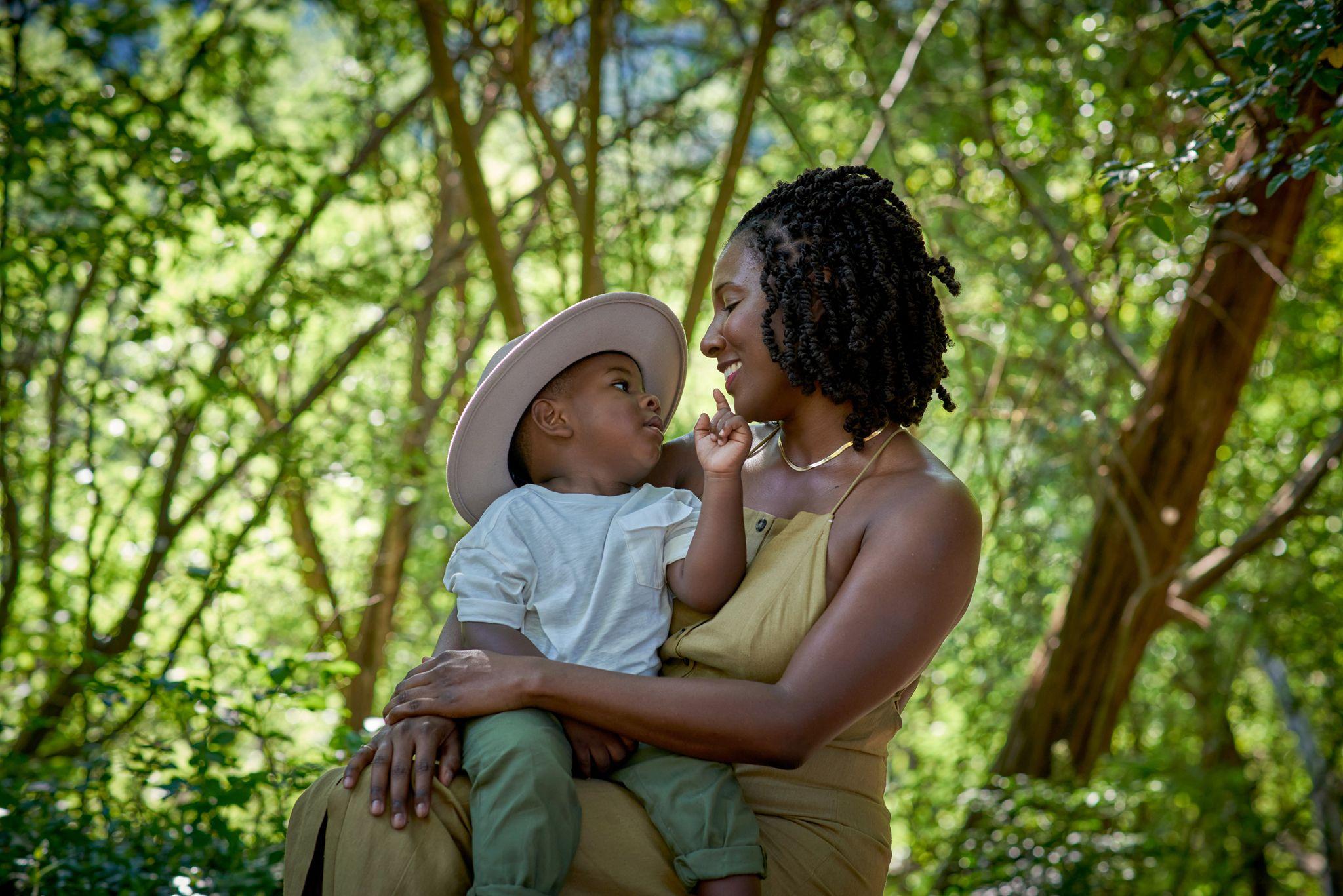 Mother in olive holding her toddler in a straw hat under the trees at Bull Creek — Bull Creek District Park photography, Austin A mother in olive holding her toddler in a straw hat under the trees at Bull Creek