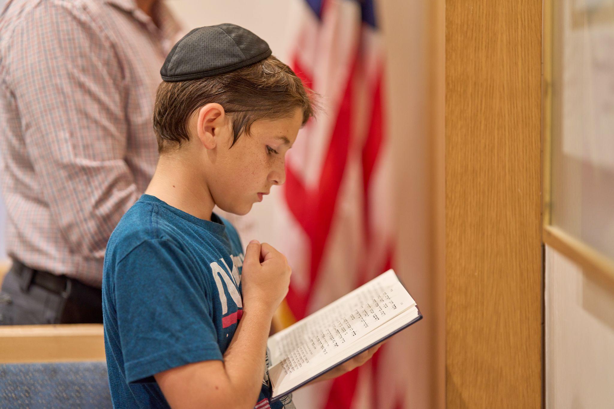 Boy in a kippah reading from a book beside a flag, preparing for his bar mitzvah — Religious Ceremonies photography, Austin A boy in a kippah reading from a book beside a flag, preparing for his bar mitzvah.