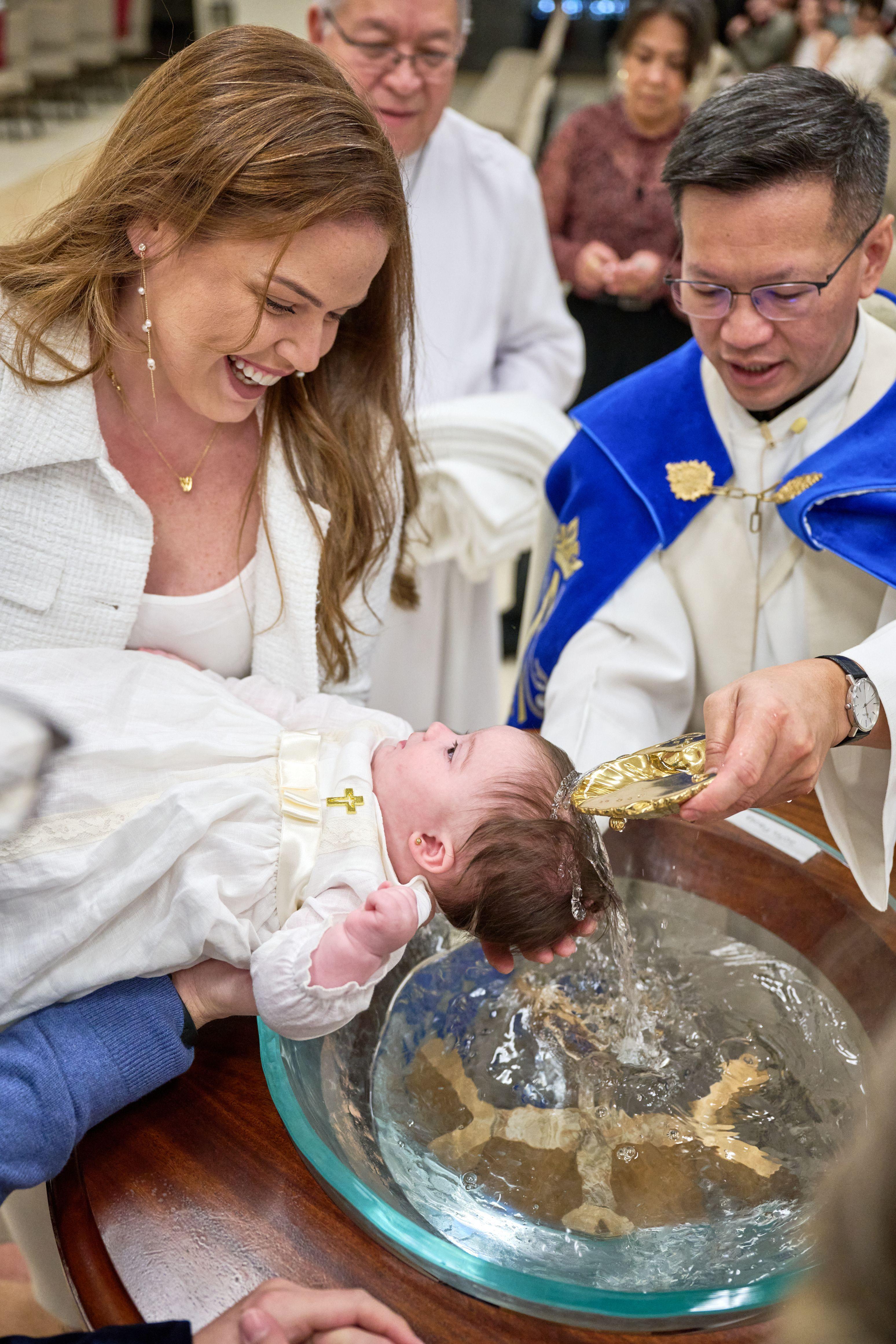 Baby held over a glass baptismal bowl by a priest in a blue and white stole — Religious Ceremonies photography, Austin A baby held over a glass baptismal bowl by a priest in a blue and white stole, the mother laughing.