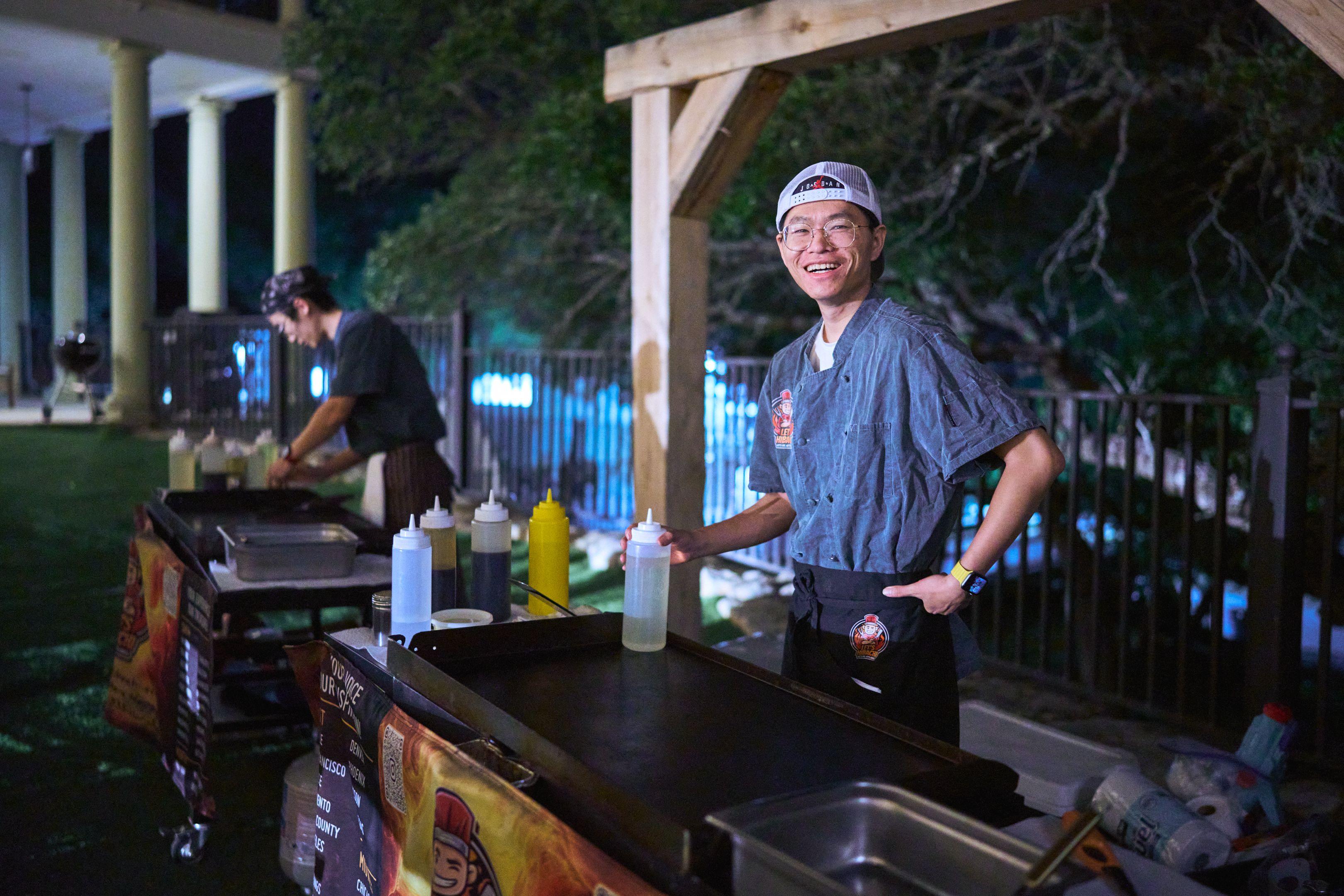 Cook working an outdoor griddle station at an evening event — Party & nightlife photography, Austin A cook working an outdoor griddle station at an evening event.