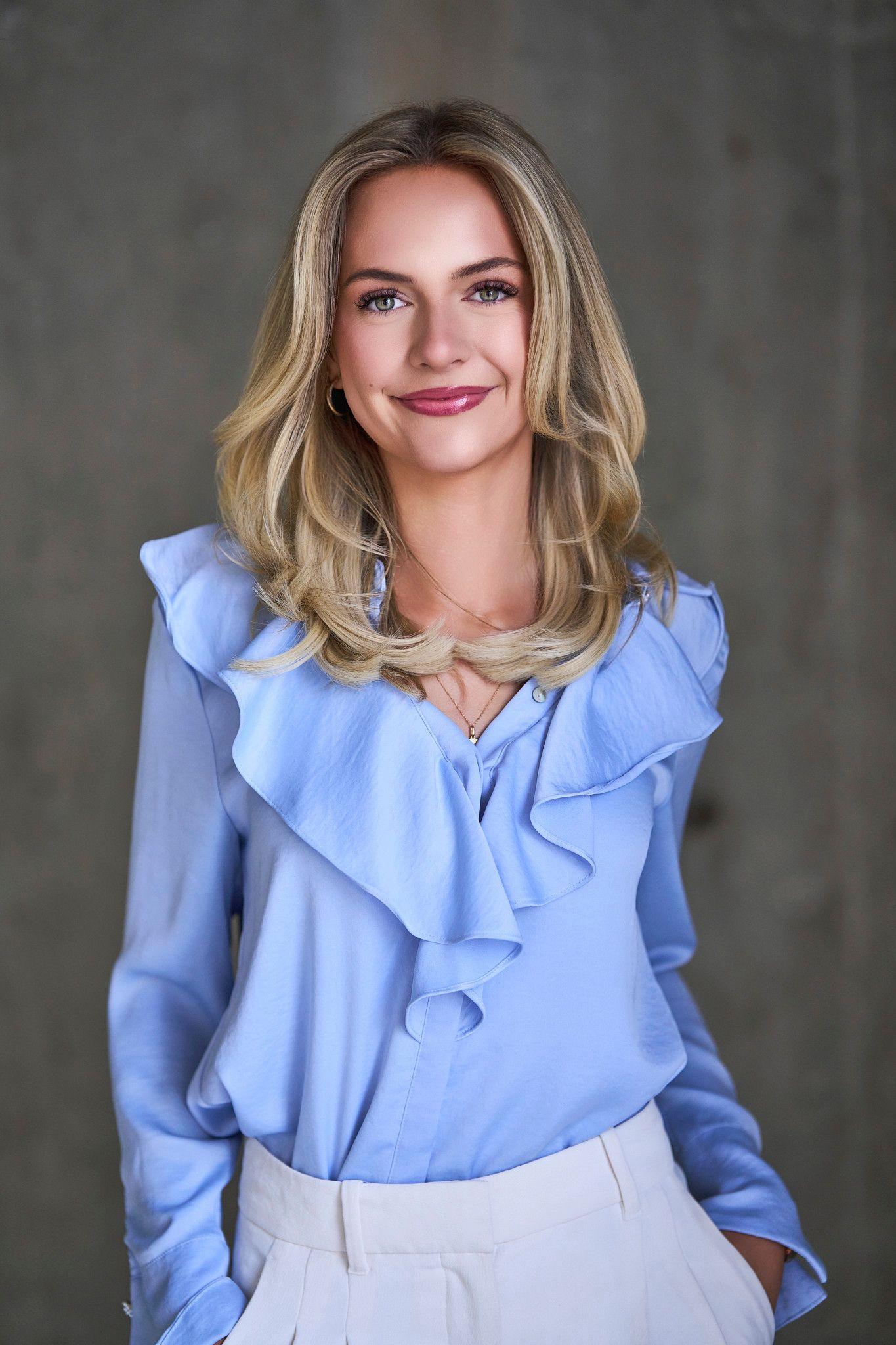Woman in a pale blue ruffled blouse smiling against a neutral wall — Photo retouching, Austin A woman in a pale blue ruffled blouse smiling against a neutral wall.