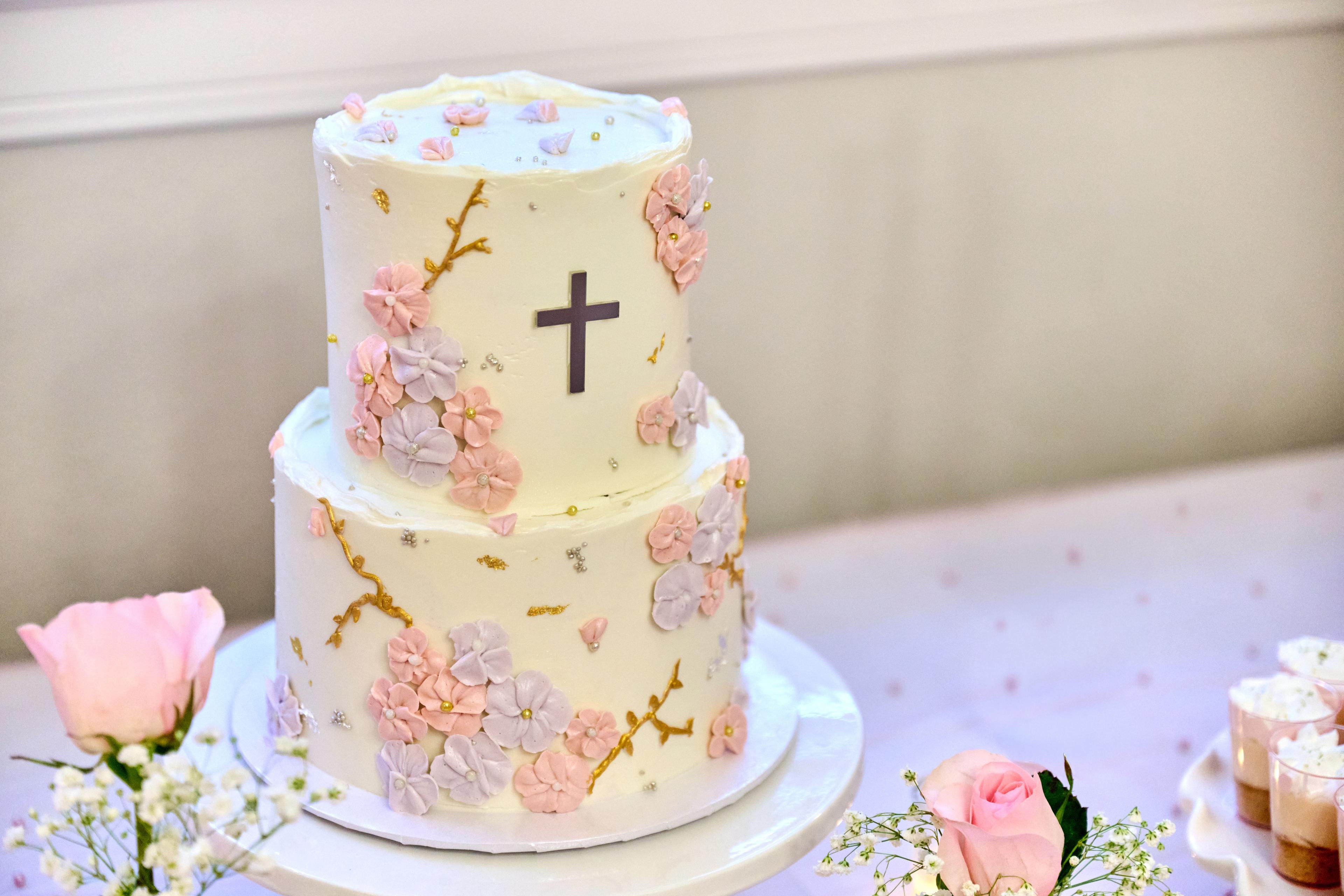 Two-tier christening cake in cream and pink, decorated with a cross and sugar flowers — Family Parties photography, Austin A two-tier christening cake in cream and pink, decorated with a cross and sugar flowers.