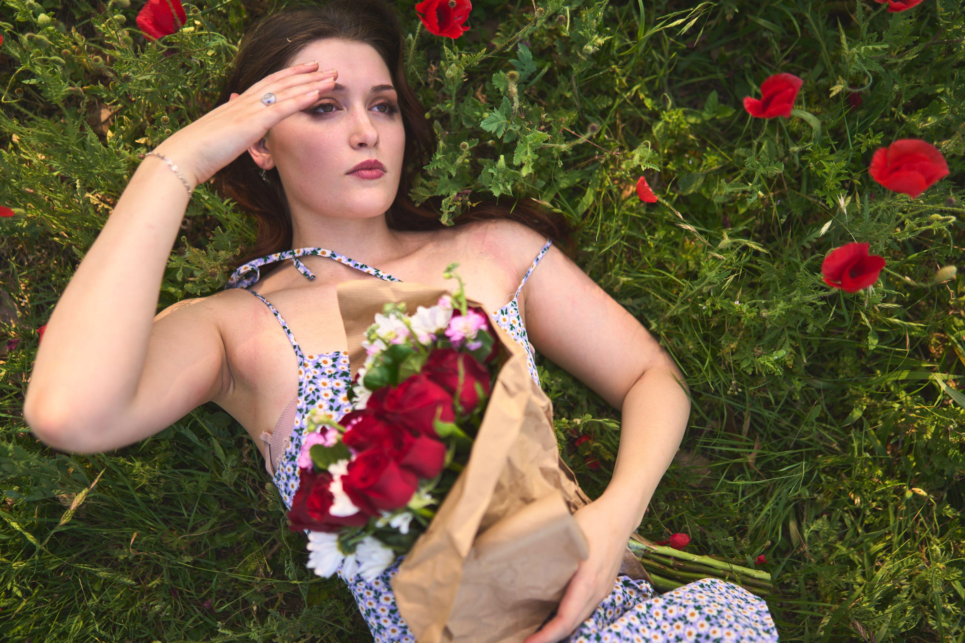 Young woman shading her eyes, lying in wildflowers beside a wrapped bouquet — Seasonal Wildflower Season in Texas photography, Austin A young woman shading her eyes, lying in wildflowers beside a wrapped bouquet.