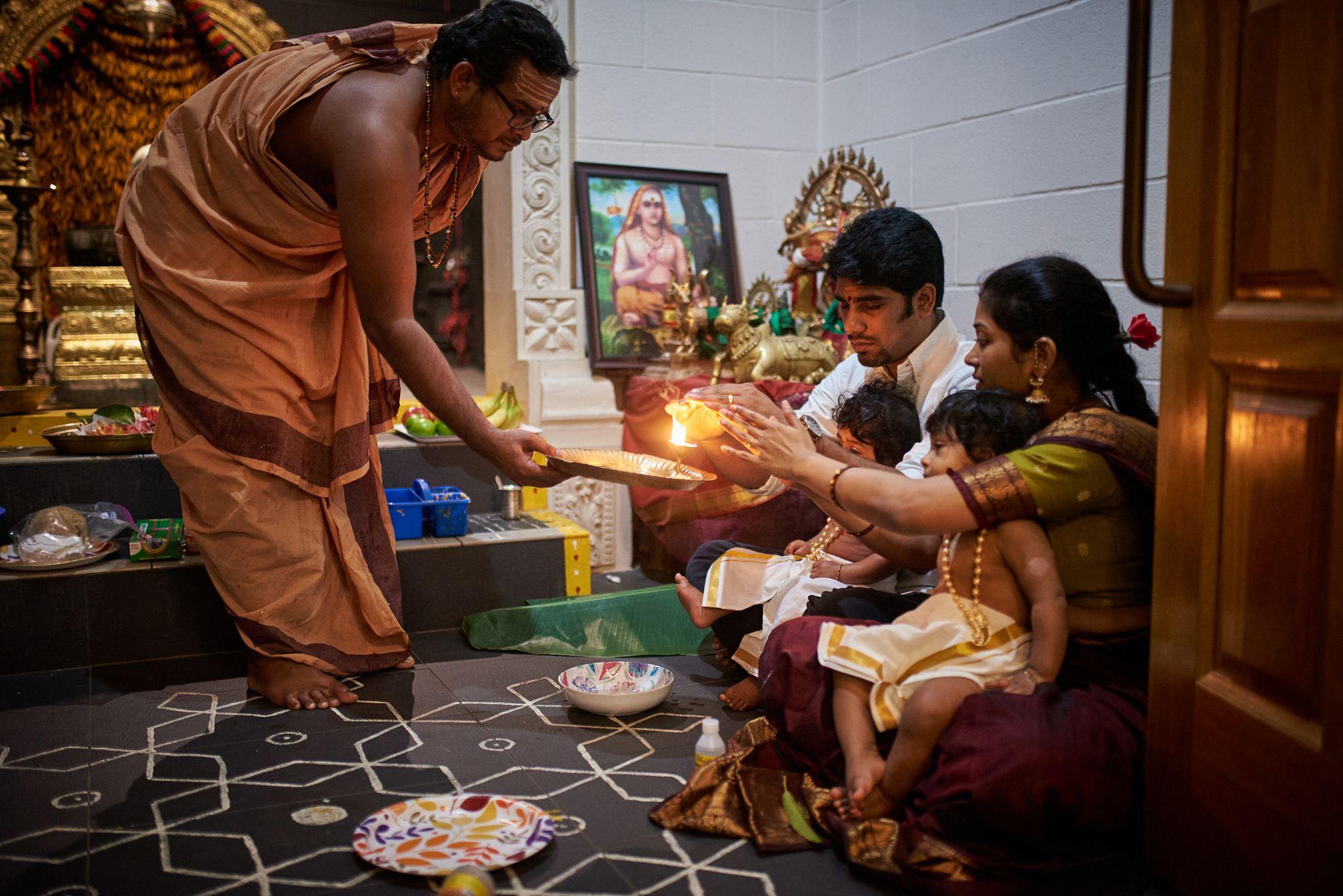 Family gathered on the floor around a home puja, an oil lamp being passed over the offerings — Religious Ceremonies photography, Austin A family gathered on the floor around a home puja, an oil lamp being passed over the offerings.