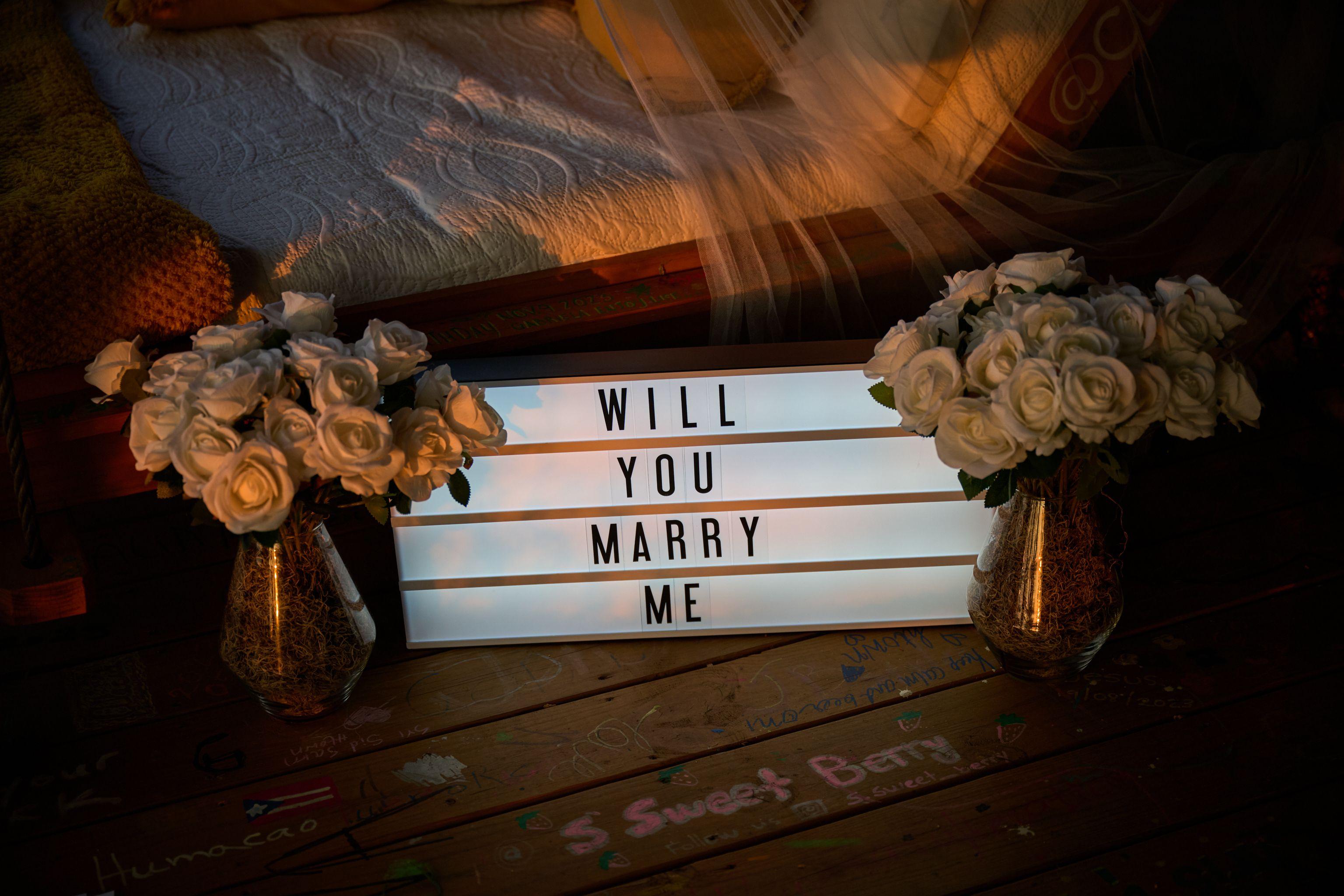 Lightbox sign reading 'WILL YOU MARRY ME' set among white roses on a wooden deck — Engagement & Proposals photography, Austin A lightbox sign reading 'WILL YOU MARRY ME' set among white roses on a wooden deck.
