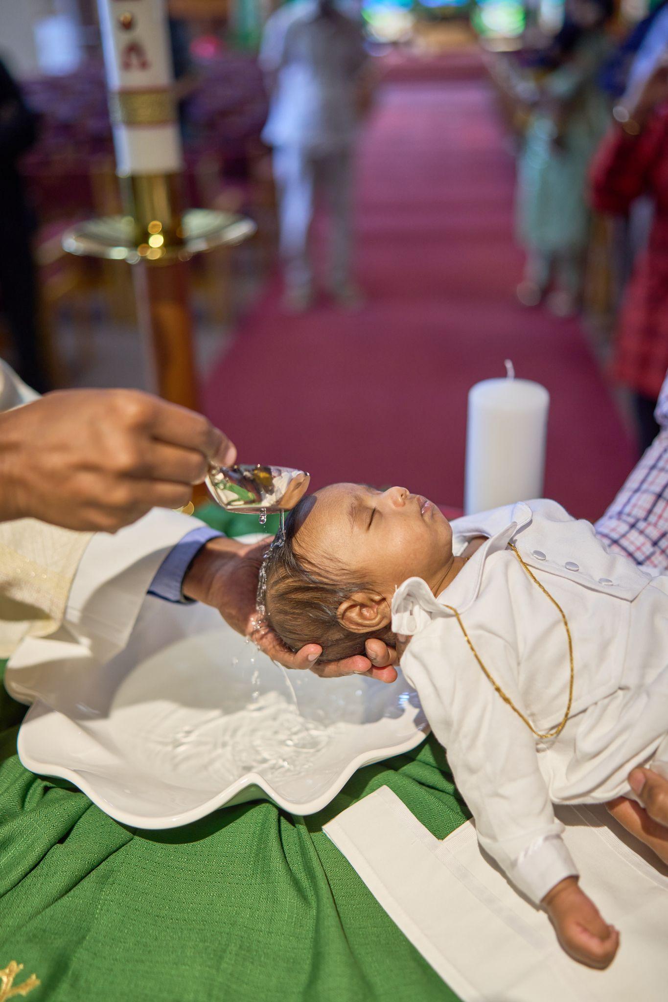 Priest anointing an infant in a white christening gown lying on a green cloth — Religious Ceremonies photography, Austin A priest anointing an infant in a white christening gown lying on a green cloth.